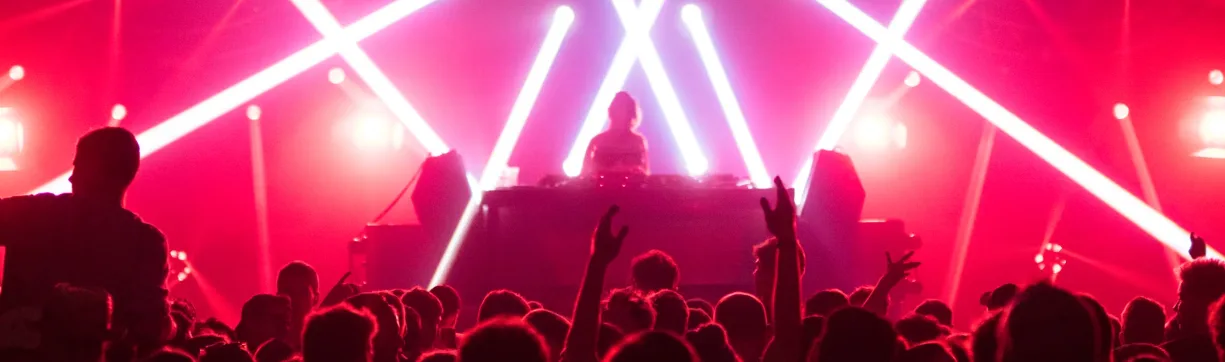 DJ performing on stage with a crowd in front and lights in the background